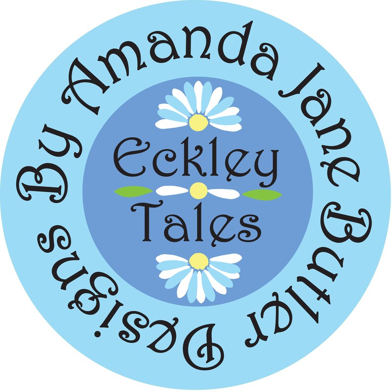 K&ouml;nnte beinhalten: Ein blauer Kreis mit wei&szlig;em Text, der "By Amanda Jane & Butter Designs." lautet. Im Inneren des Kreises befindet sich ein kleinerer Kreis mit dem Text "Eckley Tales" und drei wei&szlig;en G&auml;nsebl&uuml;mchen mit gelben Zentren.
