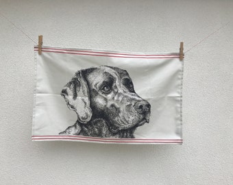 May include: A white tea towel with red trim features a black and white illustration of a Labrador Retriever's head.