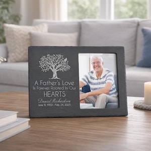 May include: A rectangular, dark gray slate picture frame with a photo of a man. The frame has a tree design and the text "A Father's Love Is Forever Rooted In Our Hearts" and the name "Daniel Richardson" with dates.
