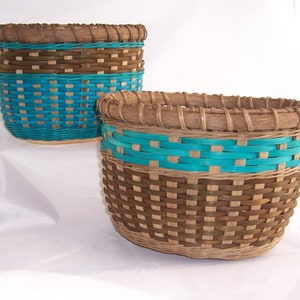 May include: Two woven baskets with a natural brown and turquoise color scheme. The baskets are cylindrical, with a woven pattern. The top and bottom sections are brown, while the middle section features a vibrant turquoise hue. The baskets are likely handmade.