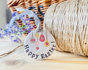 May include: White ceramic ornament with the text "Happy Easter!" and a design of colorful Easter eggs hanging from strings.