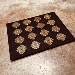 May include: A collection of 18 gold-colored metal pins with different colored gemstones in the center. Each pin features the words "Dungeon Master" around the gemstone.