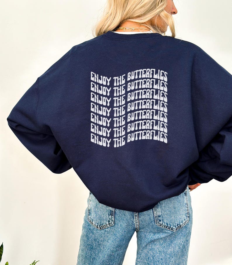 May include: A navy blue sweatshirt with the text "ENJOY THE BUTTERFLIES" repeated in a retro font on the back.