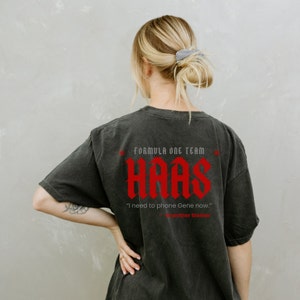 May include: Black t-shirt featuring a red graphic of the Haas Formula One team logo and the quote "I need to phone Gene now." - Guenther Steiner.