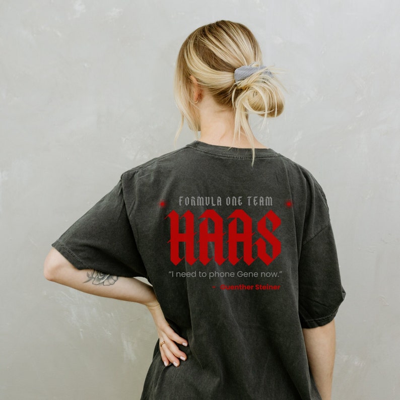 May include: Black t-shirt featuring a red graphic of the Haas Formula One team logo and the quote "I need to phone Gene now." - Guenther Steiner.