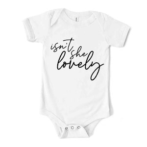May include: White baby bodysuit with short sleeves. The text "isn't she lovely" is printed in black cursive script across the front. The bodysuit has a snap closure at the bottom.
