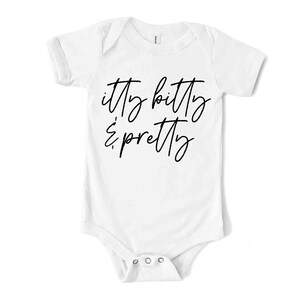 May include: White baby bodysuit with short sleeves. The text "itty bitty & pretty" is written in a cursive font across the front. The bodysuit has three poppers at the bottom.