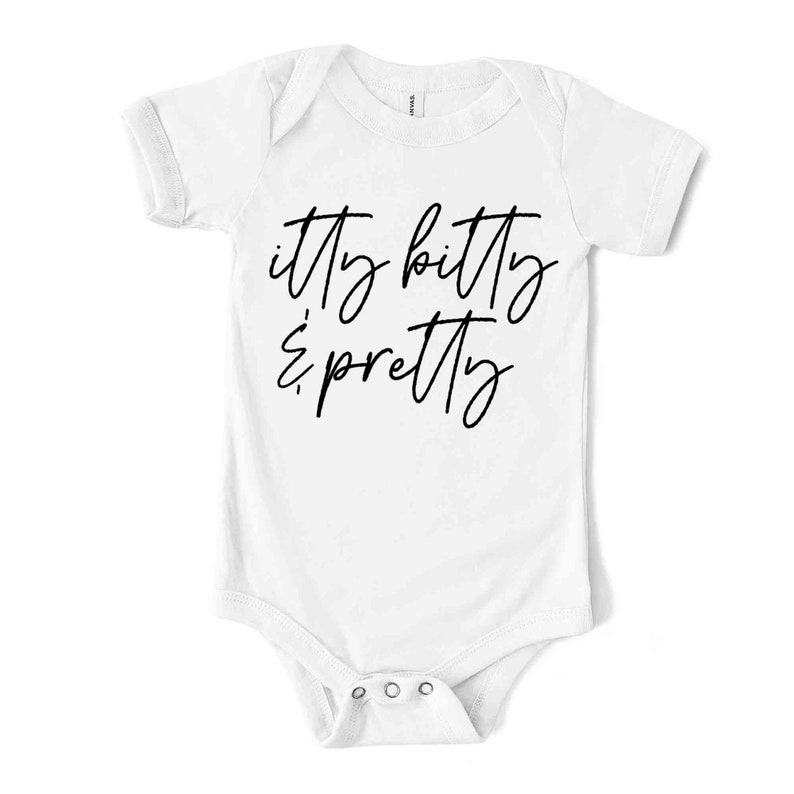 May include: White baby bodysuit with short sleeves. The text "itty bitty & pretty" is written in a cursive font across the front. The bodysuit has three poppers at the bottom.