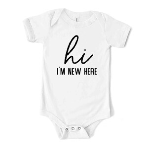 May include: White baby bodysuit with short sleeves. The text "hi I'M NEW HERE" is printed in black on the front. The bodysuit has snap closures at the bottom.