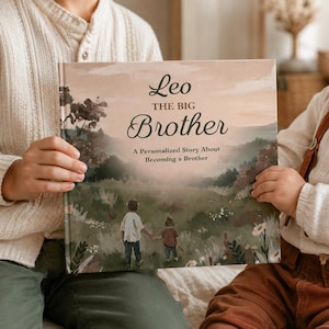 Pode incluir: Um livro de capa dura intitulado Leo The Big Brother, A Personalized Story About Becoming a Brother. A capa apresenta uma ilustração pintada em tons suaves de duas crianças caminhando por um campo de grama com árvores e céu.