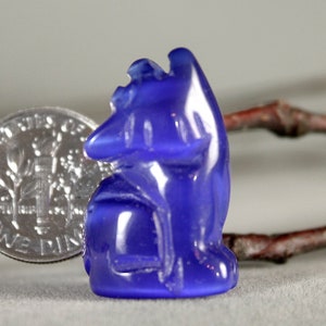 May include: A small, blue glass figurine of a cat sitting with its head tilted. The figurine is about the size of a US dime.