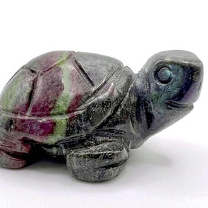 May include: A carved stone turtle figurine. The turtle's shell features a pattern of green and deep red stripes. The head and legs are a dark, iridescent gray. The figurine is a decorative item.