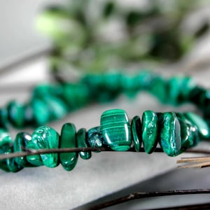 Op de afbeelding: Close-up van een armband gemaakt van gepolijste, onregelmatig gevormde malachietstenen. De stenen zijn heldergroen met donkerdere groene adering. De armband is geregen op een dunne draad.