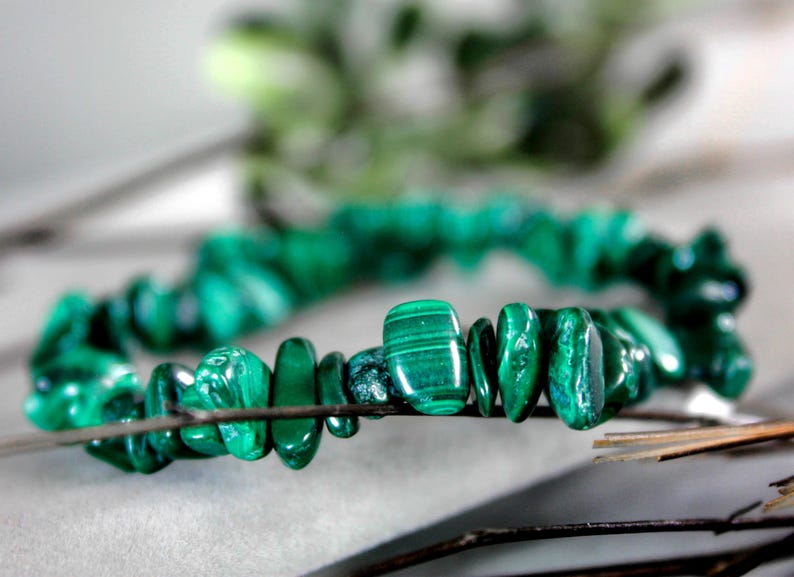 Op de afbeelding: Close-up van een armband gemaakt van gepolijste, onregelmatig gevormde malachietstenen. De stenen zijn heldergroen met donkerdere groene adering. De armband is geregen op een dunne draad.