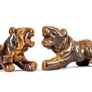 May include: Two carved tiger figurines in shades of brown and amber are displayed against a white background. The tigers are posed in a roaring stance, showcasing detailed craftsmanship. These decorative sculptures are ideal for home decor.