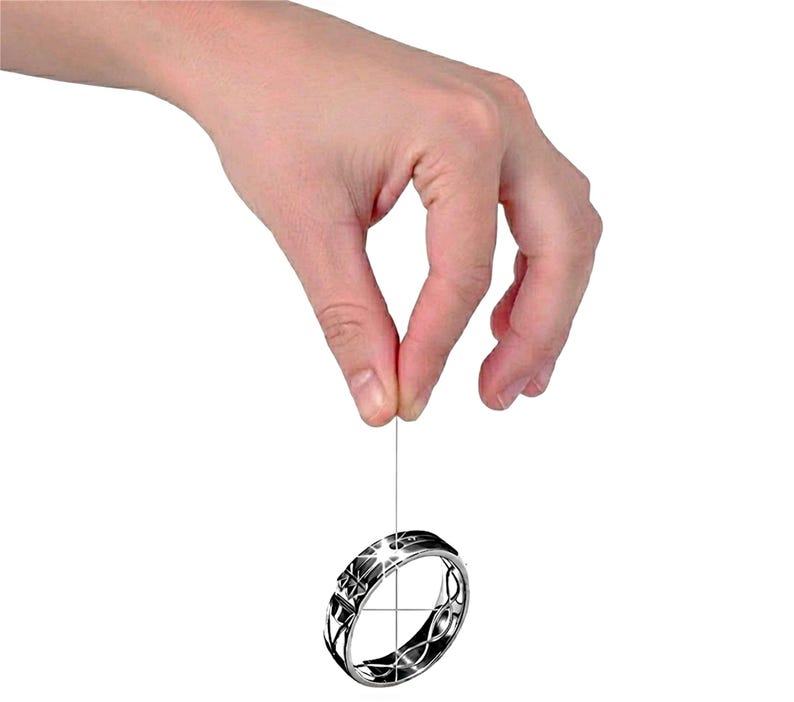 Op de afbeelding: Een zilveren ring met een geometrisch ontwerp hangt aan een dunne draad. De ring heeft ingewikkelde patronen en een gepolijste afwerking, die licht reflecteert. Het ontwerp van de ring omvat stervormige vormen en gebogen lijnen.