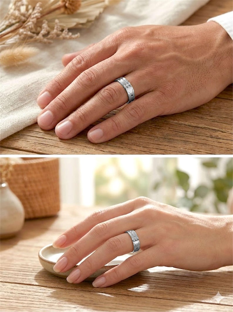 Op de afbeelding: Zilverkleurige ring met een hartvormig ontwerp en een getextureerde band. De ring wordt op twee handen getoond, wat suggereert dat het een partnerring is. De ring wordt gepresenteerd op een houten oppervlak.