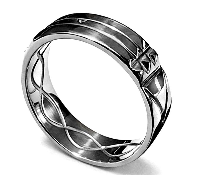 Op de afbeelding: Een zilveren ring met een gedetailleerd ontwerp. De ring heeft een reeks parallelle lijnen over de bovenkant en een ingewikkeld patroon aan de zijkanten. De ring heeft een gepolijst, reflecterend oppervlak.