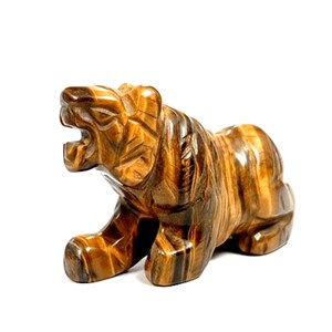 May include: A tiger's eye stone carving of a tiger in a roaring stance. The figurine features detailed carving of the tiger's fur and facial features. The stone has brown and gold bands.