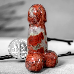 May include: A red and white carved stone sculpture in the shape of a human body part. The sculpture is about the size of a U.S. dime.