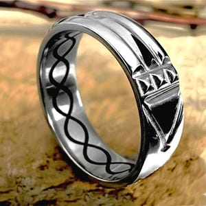 Op de afbeelding: Een zilveren ring met een geometrisch ontwerp. De ring heeft verhoogde lijnen en een driehoekig patroon. De binnenkant van de ring heeft een zwart oneindigheidssymboolontwerp. De ring wordt gepresenteerd op een houten oppervlak.
