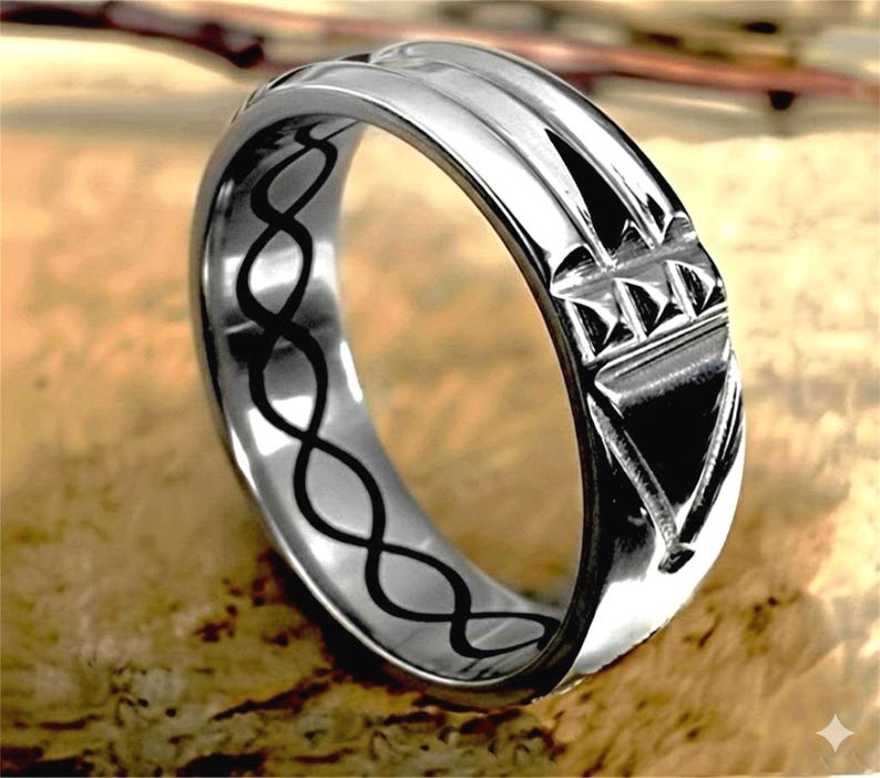 Op de afbeelding: Een zilveren ring met een geometrisch ontwerp. De ring heeft verhoogde lijnen en een driehoekig patroon. De binnenkant van de ring heeft een zwart oneindigheidssymboolontwerp. De ring wordt gepresenteerd op een houten oppervlak.