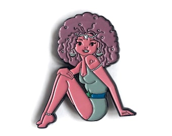 May include: A pink and purple enamel pin of a cartoon woman with a large afro, wearing a green swimsuit and a star on her forehead. She is holding a scale in each hand. The pin is a representation of the zodiac sign Libra.