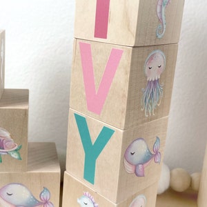 May include: Wooden blocks spelling the name "IVY" with a seahorse, whale, and jellyfish design on each block.