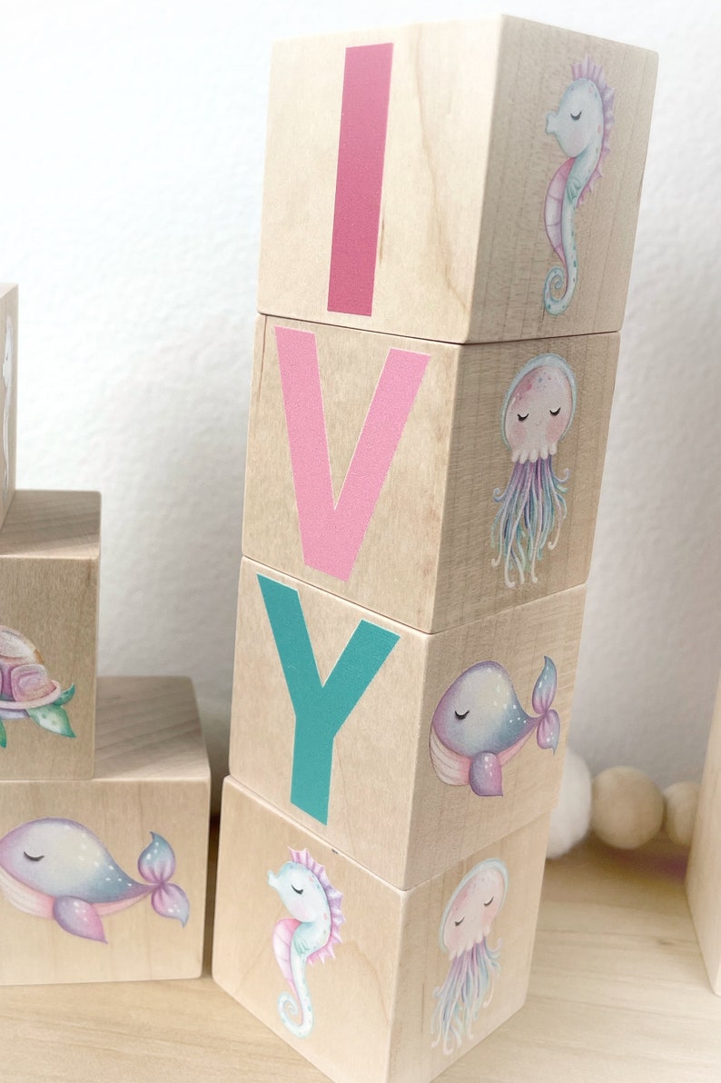 May include: Wooden blocks spelling the name "IVY" with a seahorse, whale, and jellyfish design on each block.