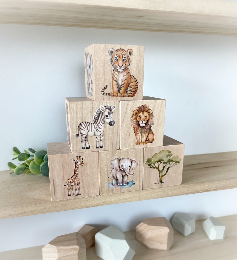 May include: Wooden blocks with painted images of a tiger, zebra, lion, giraffe, elephant, and a tree. The blocks are stacked in a pyramid shape.