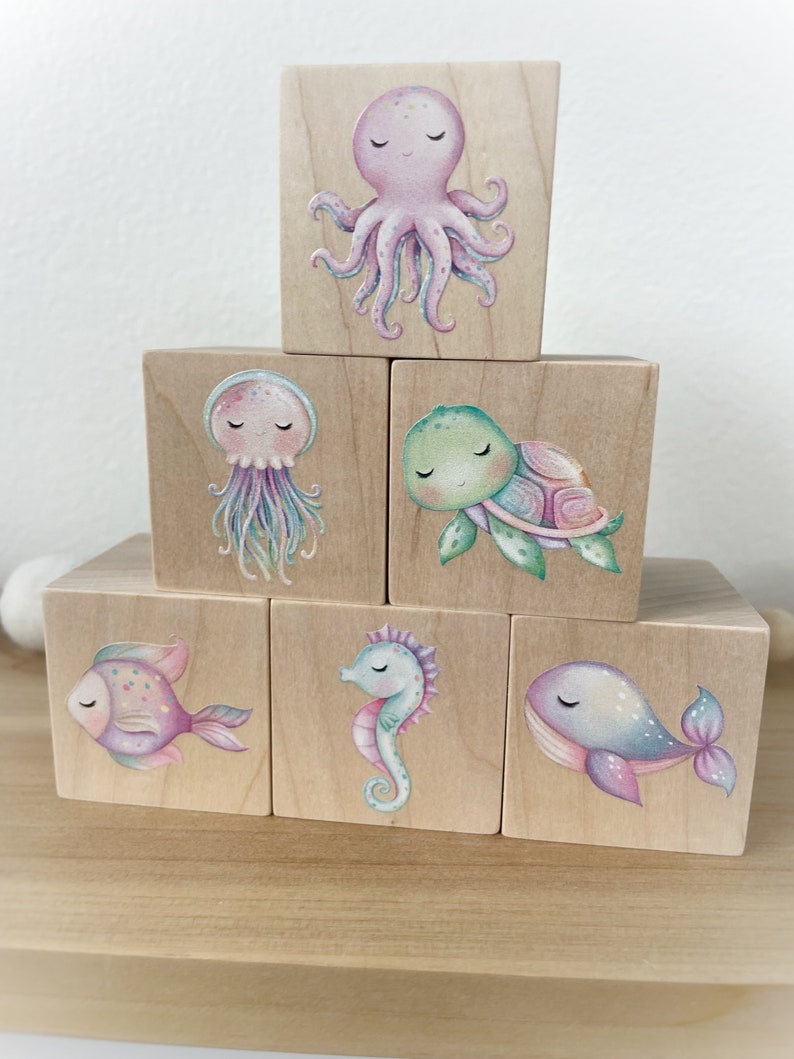 May include: Six wooden blocks with colorful illustrations of sea creatures. The blocks feature an octopus, a jellyfish, a turtle, a fish, a seahorse, and a whale.