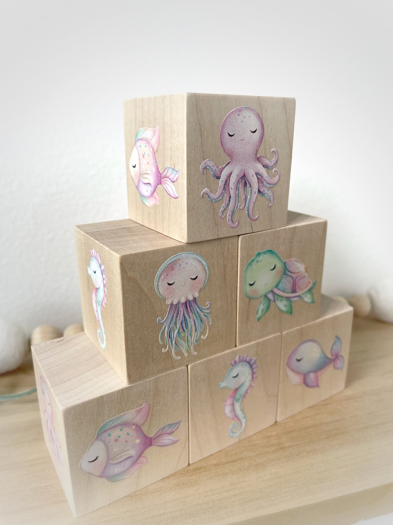 May include: A set of wooden blocks with colorful illustrations of sea creatures, including a fish, octopus, jellyfish, turtle, whale, and seahorse. The blocks are stacked in a pyramid shape.