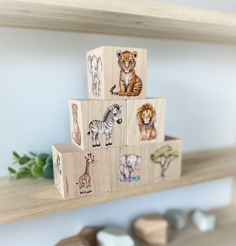 May include: A set of wooden blocks featuring different safari animals, including a zebra, giraffe, lion, elephant, and tiger. The blocks are stacked in a pyramid shape.