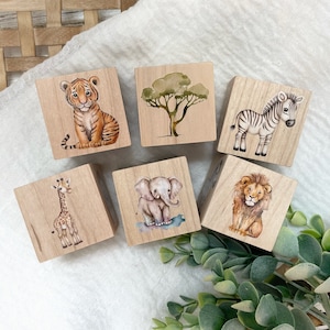 May include: Six wooden blocks with painted images of animals and a tree. The animals include a tiger, zebra, giraffe, elephant, and lion. The tree is green and has a brown trunk.