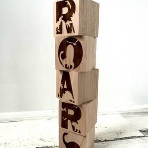 以下が含まれることがあります： 恐竜のシルエットとヤシの木が描かれた木製のブロックで「ROAR」という単語を綴っています。