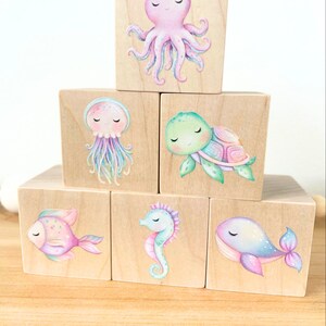 May include: Six wooden blocks with colorful illustrations of sea creatures. The blocks feature an octopus, a jellyfish, a turtle, a fish, a seahorse, and a whale.