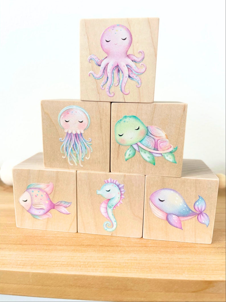 May include: Six wooden blocks with colorful illustrations of sea creatures. The blocks feature an octopus, a jellyfish, a turtle, a fish, a seahorse, and a whale.
