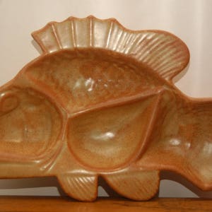 Könnte beinhalten: Eine Keramik-Servierplatte in Fischform mit drei unterteilten Abschnitten. Die Platte ist in einem hellbraunen Ton glasiert und hat eine gesprenkelte Oberfläche.