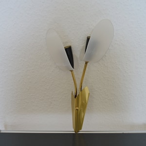 Puede incluir: Un par de apliques de pared doradas con pantallas de vidrio blanco esmerilado. Las apliques tienen forma de flores estilizadas con un solo tallo y dos hojas.