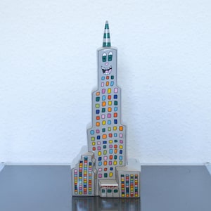 Könnte beinhalten: Ein farbenfroher Wolkenkratzer im Cartoon-Stil mit einem lächelnden Gesicht und einem grün-weiß gestreiften Dach. Das Gebäude ist aus Holz und mit verschiedenen Farben bemalt, darunter Rot, Blau, Grün, Gelb und Pink.