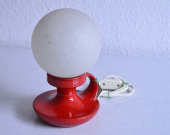 May include: A red ceramic table lamp with a white frosted glass globe shade. The lamp has a simple design with a curved base and a single switch on the cord.