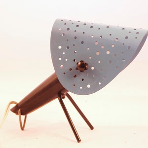 Könnte beinhalten: Eine blaue Tischlampe aus Metall mit einem perforierten Schirm und einem schwarzen Metallfuß mit drei Beinen.