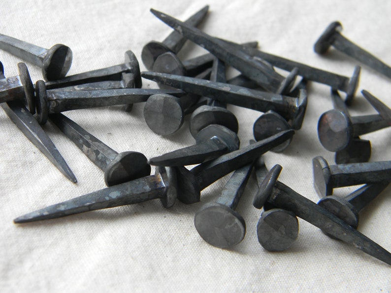 Puede incluir: Una colecci&oacute;n de clavos antiguos forjados a mano con cabezas redondeadas. Los clavos son de metal y tienen un acabado gris oscuro.