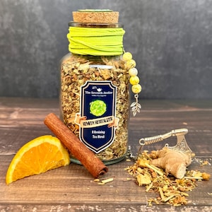 May include: A glass jar filled with a tea blend, labeled "Remedy Revitalizer." The jar is adorned with a yellow ribbon and a cork stopper. Accompanying the jar are a cinnamon stick, an orange slice, and a small decorative axe.
