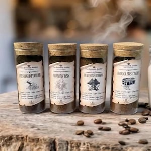 May include: Four glass jars with cork lids filled with coffee grounds. Each jar has a label with a pirate-themed design and text. The labels read "Fresh Gunpowder", "Parakeens Kiss", "Dead Man's Remains", and "Smugglers Cache".
