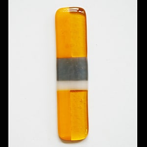 May include: A rectangular, fused glass piece with a gradient of colors. The top and bottom sections are amber, separated by a gray and white band. The glass has a glossy finish and is set against a white background.