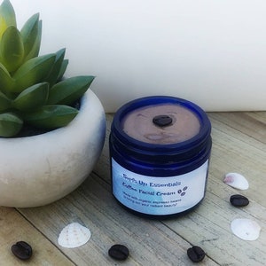 Może przedstawiać: Niebieski słoik z kawowym kremem do twarzy z brązową pokrywką. Słoik jest oznaczony etykietą "Surf's Up Essentials Coffee Facial Cream" i "Made with organic espresso beans to bring out your radiant beauty!"