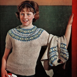Peut inclure: Un pull en tricot beige avec un empiècement à motifs bleu, jaune et blanc. Un cardigan assorti est drapé sur le bras. La personne tient une pochette de disque rouge et blanche.