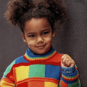 May include: A young girl with curly brown hair wears a colourful knitted jumper with a patchwork design. The jumper is made of squares in red, yellow, blue, and green.