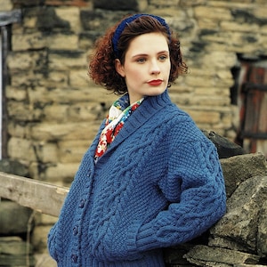 May include: A blue knitted cardigan with a cable knit pattern and a shawl collar. The cardigan has buttons down the front and is worn over a floral scarf.